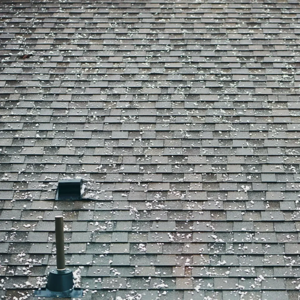 Close-up of a rooftop with gray shingles partially covered in scattered hailstone