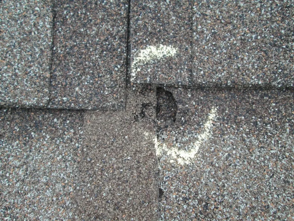 Close-up of asphalt shingles on a roof, featuring a circled damaged area marked in white